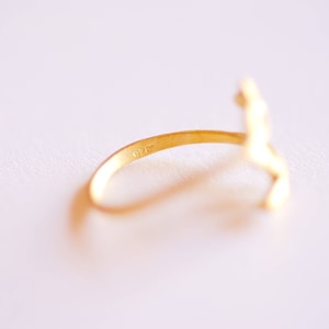 May include: A gold ring with a stylized figure design. The ring is marked with the number "925" on the inside band.