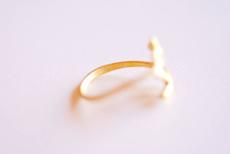 May include: A gold ring with a stylized figure design. The ring is marked with the number "925" on the inside band.