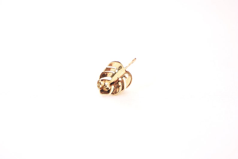 May include: A gold-colored earring featuring a detailed monstera leaf design.