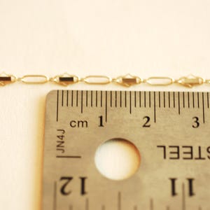 May include: A gold chain necklace with a delicate, oval-shaped link pattern. The chain is measured against a ruler, showing it is approximately 2 inches long.