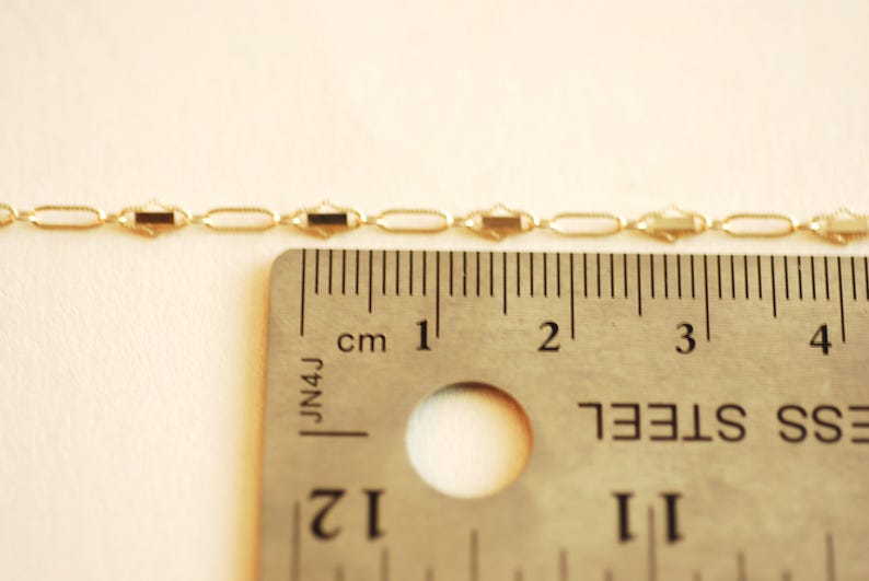 May include: A gold chain necklace with a delicate, oval-shaped link pattern. The chain is measured against a ruler, showing it is approximately 2 inches long.