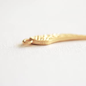 May include: A gold-colored wing charm with a textured surface. The charm has a loop for attaching to a necklace or bracelet. The charm is marked with the number "925".