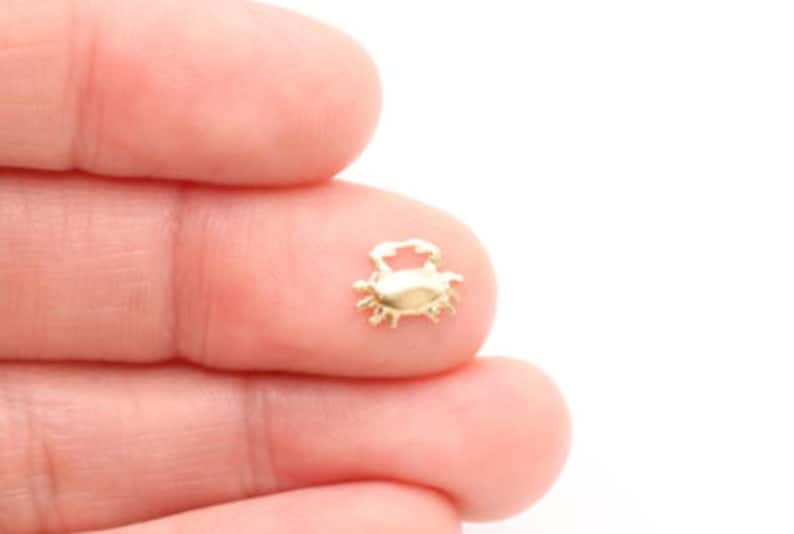 K&ouml;nnte beinhalten: Ein kleiner goldener Krabben-Anh&auml;nger, perfekt, um Schmuck oder Bastelarbeiten mit einem Hauch von Verspieltheit zu versehen.