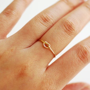 May include: A gold knot ring on a finger.