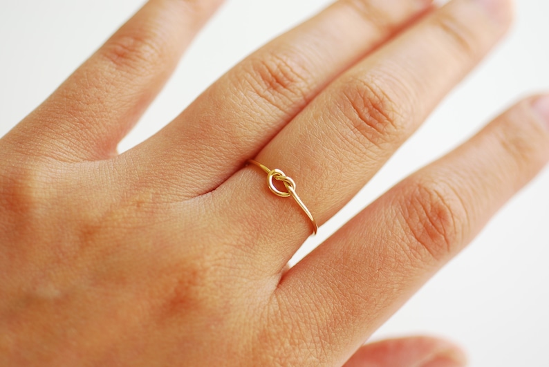 May include: A gold knot ring on a finger.