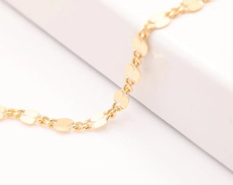 May include: A delicate gold-colored necklace featuring a chain of small, flat, circular charms. The necklace is displayed against a white background, highlighting its simple elegance. This jewelry piece is suitable for everyday wear.