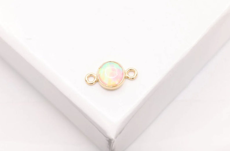 May include: Gold connector with a round opal-like stone in the center. The connector has two loops on either side.