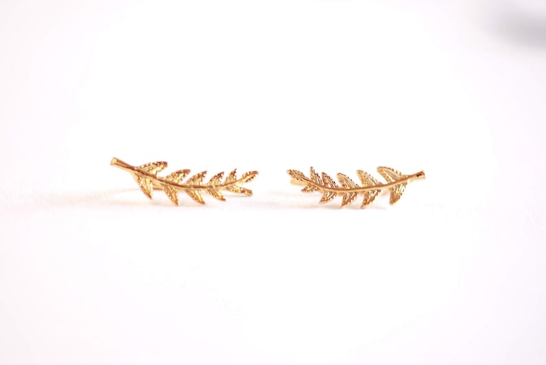 May include: A pair of gold leaf ear cuffs. The cuffs are shaped like a branch of leaves and are curved to fit the ear.