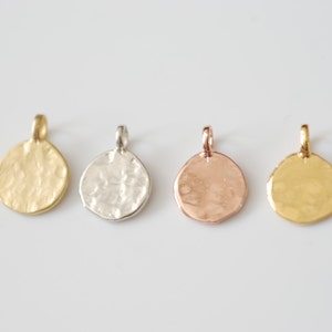 Pode incluir: Quatro pingentes redondos de metal em diferentes cores: ouro, prata, ouro rosa e latão. Cada pingente tem uma textura martelada e um laço para prender a uma corrente.