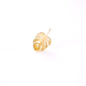 May include: A gold-colored metal leaf cutout in the shape of a monstera plant.