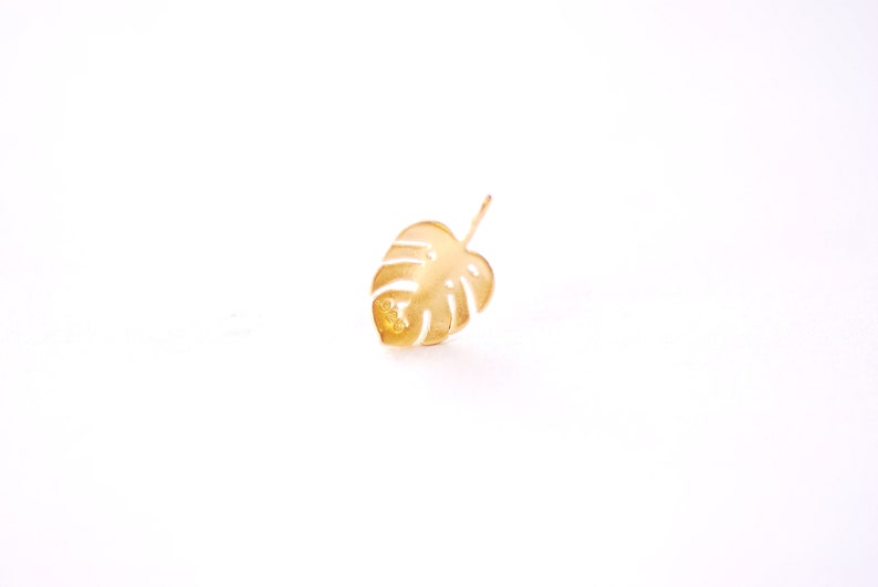 May include: A gold-colored metal leaf cutout in the shape of a monstera plant.
