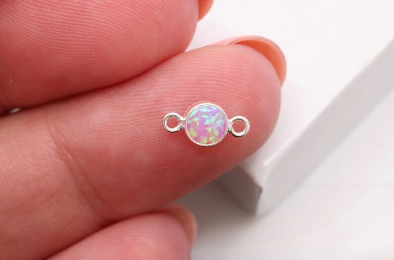May include: A silver connector with a round, iridescent opal-like stone in the center. The connector has two loops on either side of the stone.