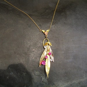 May include: A gold necklace with a pendant featuring a cluster of pink and clear stones set in a leaf design.