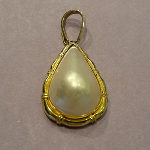 May include: A gold pendant with a large white pearl in a teardrop shape.