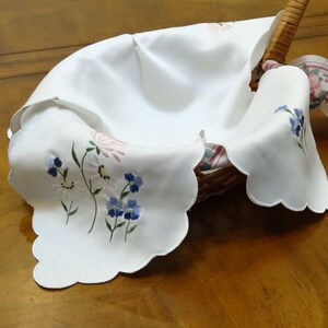 May include: White embroidered fabric basket liner with scalloped edges and floral designs in blue, pink, and green.