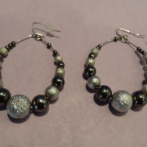 May include: A pair of hoop earrings with a mix of silver and black beads. The earrings feature a silver hook and are composed of various sized beads, creating a stylish accessory.