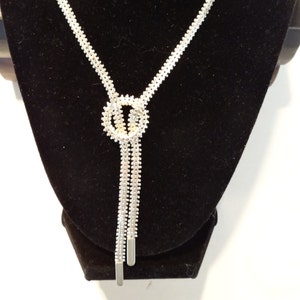 May include: A silver necklace with a knot design and a long, dangling chain.