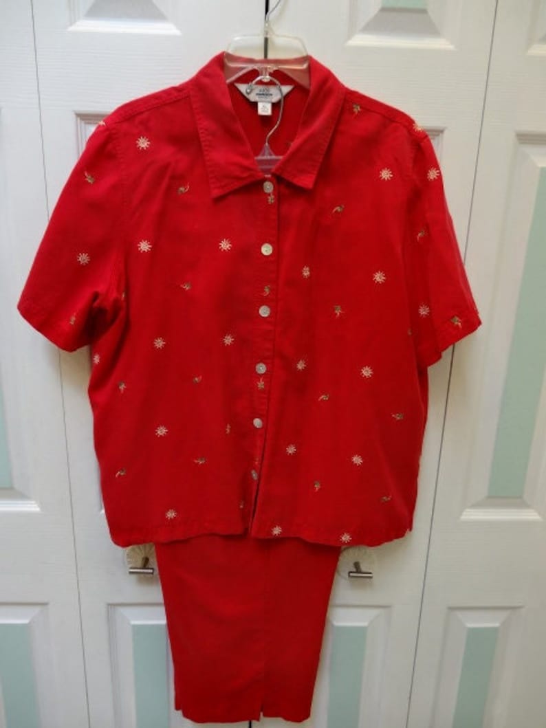 May include: A red button-down shirt with a floral pattern and matching red trousers. The shirt has a collar and short sleeves. The trousers have a straight leg.