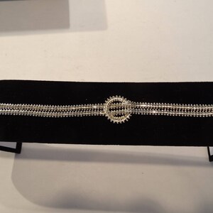 May include: A silver bracelet with a circular design in the center. The bracelet is made of multiple strands of small beads.