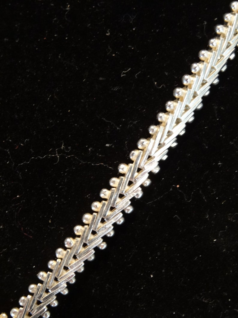 May include: A silver chain necklace with a geometric pattern. The chain is made of small, interconnected links that form a repeating pattern of triangles.