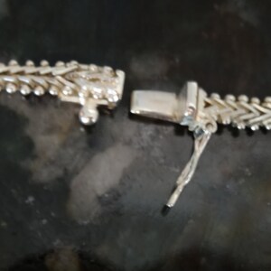 May include: A silver chain necklace with a lobster clasp closure. The chain is made of small, interlocking links that form a herringbone pattern.