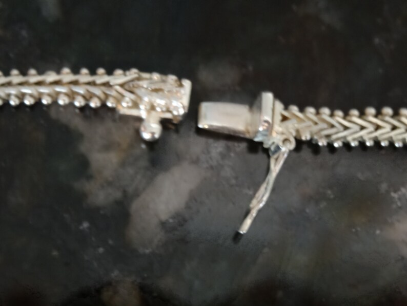 May include: A silver chain necklace with a lobster clasp closure. The chain is made of small, interlocking links that form a herringbone pattern.