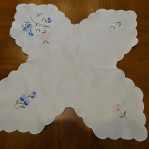 May include: White scalloped edge table runner with embroidered blue and pink flowers.