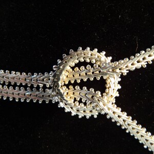 May include: A silver chain necklace with a decorative knot design. The chain is made of small, interlocking links.