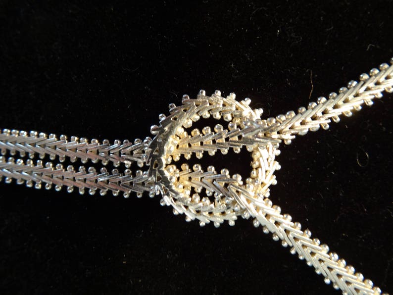 May include: A silver chain necklace with a decorative knot design. The chain is made of small, interlocking links.