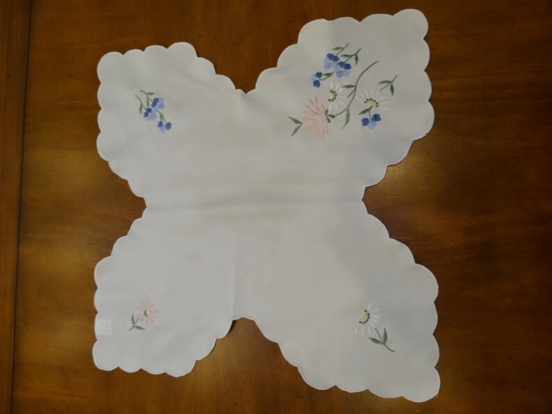 May include: White embroidered table runner with a scalloped edge and floral designs in pink, blue, and green.