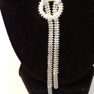 May include: A silver chain necklace with a knot design and two long strands. The necklace is displayed on a black velvet stand.
