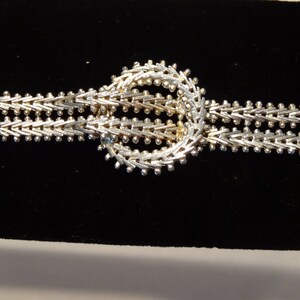 May include: A silver chain bracelet with a unique, circular, interlocking design. The chain is made of small, linked, silver beads.