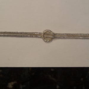 May include: A silver bracelet with a circular design in the center. The bracelet is made of two rows of linked metal pieces.