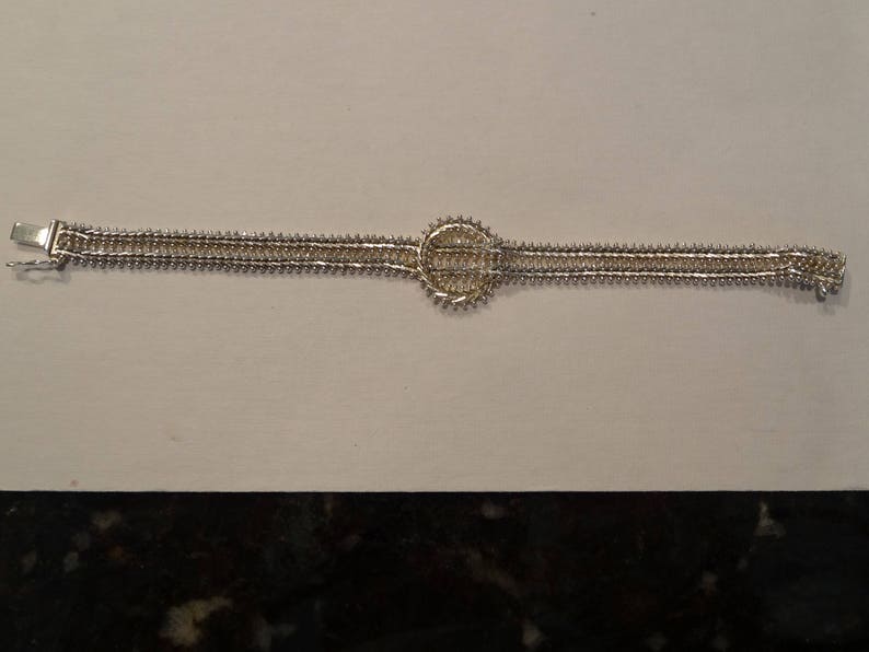 May include: A silver bracelet with a circular design in the center. The bracelet is made of two rows of linked metal pieces.