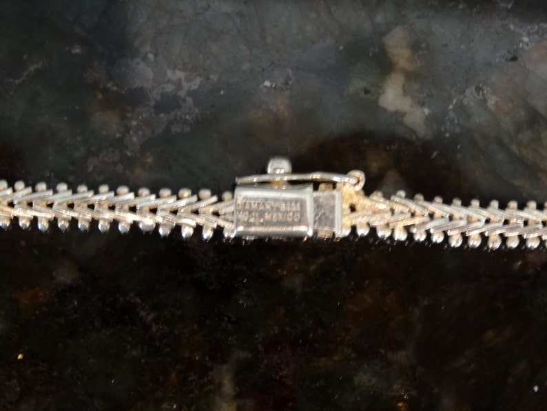May include: Close-up of a silver chain with a clasp that reads "STERLING 925 ITALY MEXICO".