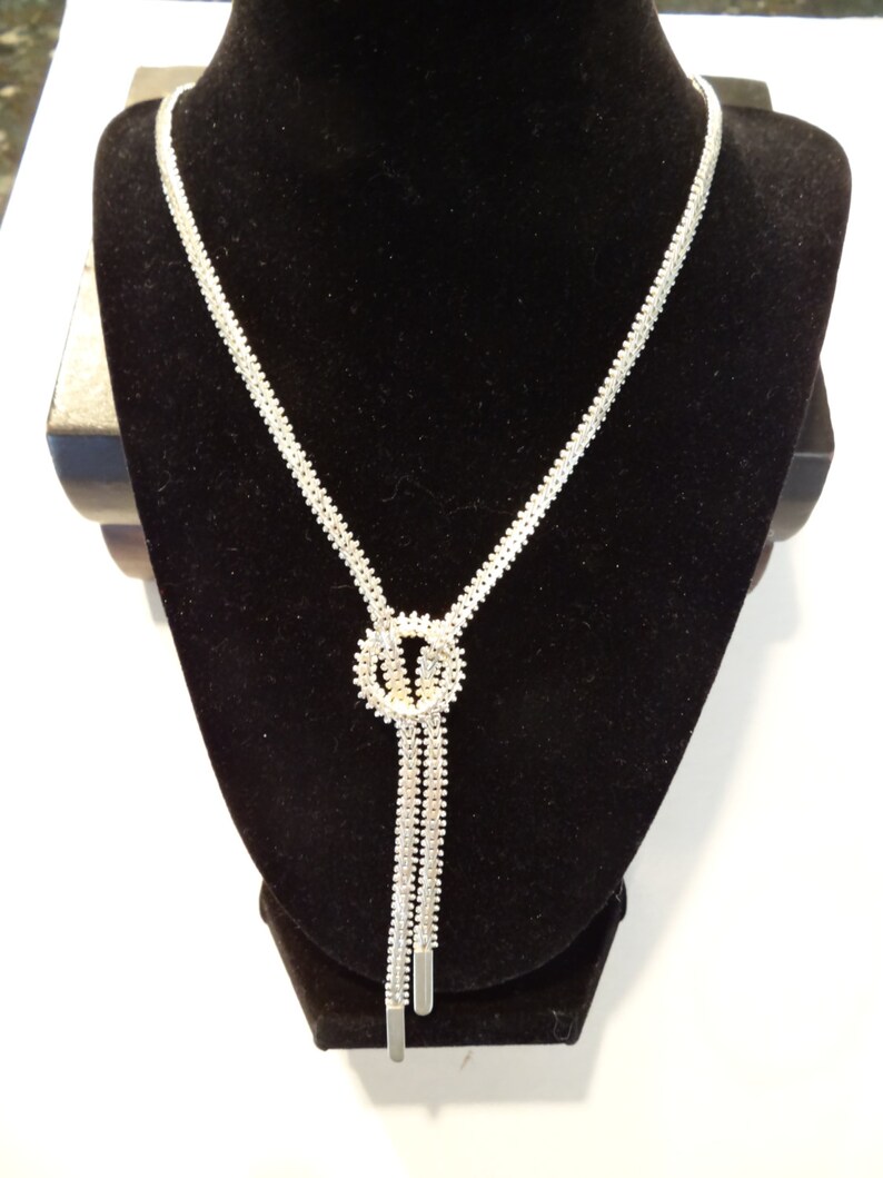 May include: A silver necklace with a knot design and a long, dangling chain.