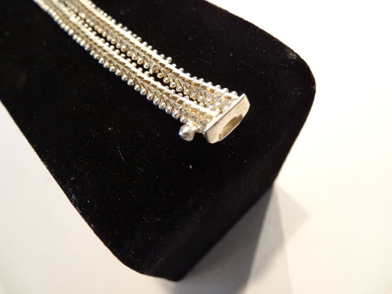 May include: A silver chain necklace with a delicate, layered design. The chain is made of small, round beads that are connected in a repeating pattern.