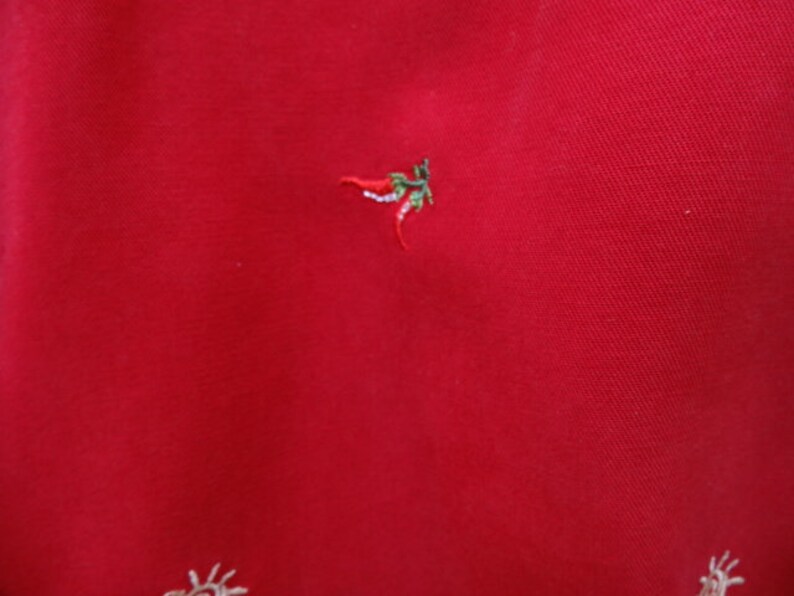 May include: A red fabric background with a small embroidered chili pepper design.