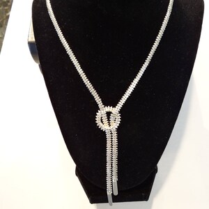 May include: A silver chain necklace with a knot design and a small circle pendant. The necklace is on a black velvet display stand.
