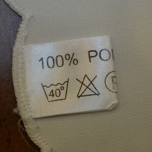 May include: White fabric label with black text that reads "100% POLY" and a washing instruction icon that says "40&deg;".