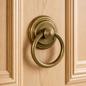 Peut inclure: Gros plan d'un heurtoir de porte en laiton antique avec une poignée en forme d'anneau circulaire. Le heurtoir est monté sur une porte en bois de couleur claire avec des panneaux verticaux et des garnitures décoratives.