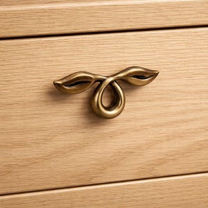 Peut inclure: Gros plan sur une poignée de tiroir en laiton avec un design en forme de feuille. La poignée est montée sur un tiroir en bois de couleur claire. La quincaillerie a une forme décorative unique, ajoutant une touche d'élégance au meuble.