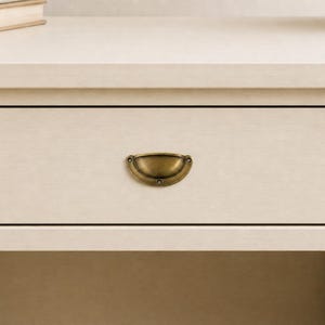 Peut inclure: Une table de chevet crème avec un seul tiroir et une poignée en laiton. Le tiroir est centré et présente un design simple et élégant. La table de chevet a une étagère sous le tiroir et un dessus plat.