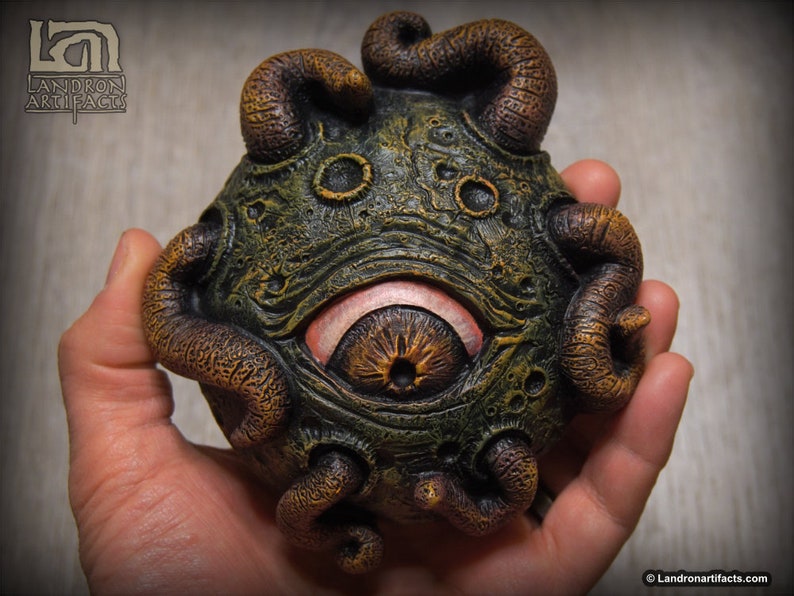 May include: A green and brown, hand-painted, ceramic sculpture of a creature with a large eye and tentacles. The sculpture is about the size of a person's hand.