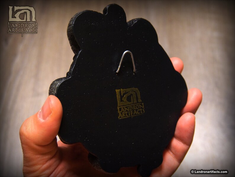 May include: Black wall hanging with a gold logo that reads "Landron Artifacts". The wall hanging has a metal hook on the back.