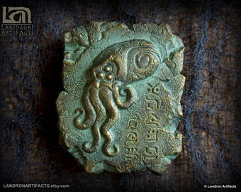 May include: A green and gold metal plaque with a raised relief sculpture of a tentacled creature. The plaque has an inscription in an unknown language.
