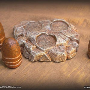 May include: A collection of handcrafted, brown and tan stone-like objects. The centerpiece is a textured, irregularly shaped item with two circular indentations. Three smaller, cylindrical pieces with horizontal bands are also present.