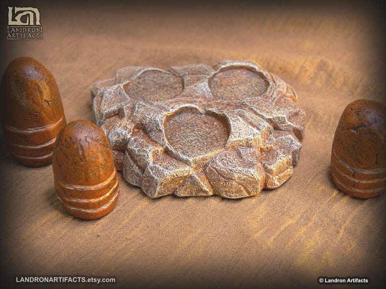 May include: A collection of handcrafted, brown and tan stone-like objects. The centerpiece is a textured, irregularly shaped item with two circular indentations. Three smaller, cylindrical pieces with horizontal bands are also present.