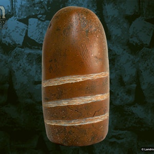 May include: A brown, elongated, smooth stone with white lines carved into it. The stone is about 10 inches long and 3 inches wide.