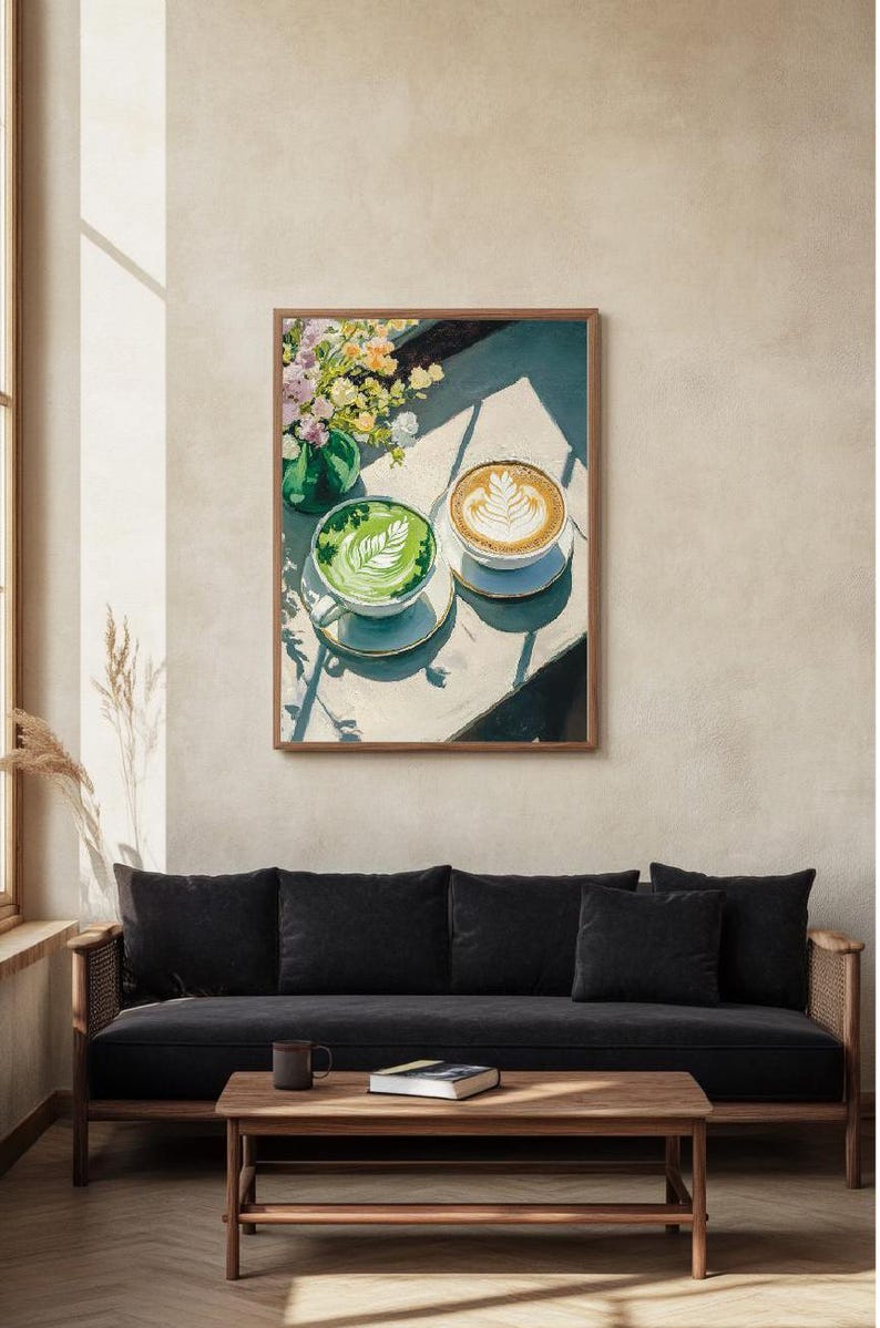 May include: A framed painting of two cups of coffee on a table. One cup is green and the other is brown with latte art. The cups are on a white table with a vase of flowers in the background.